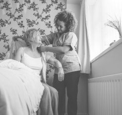 caregiver assisting elder woman on wearing a shirt